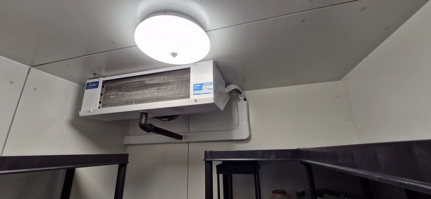 Verdamper met leidingaansluitingen boven rekken in een koelruimte