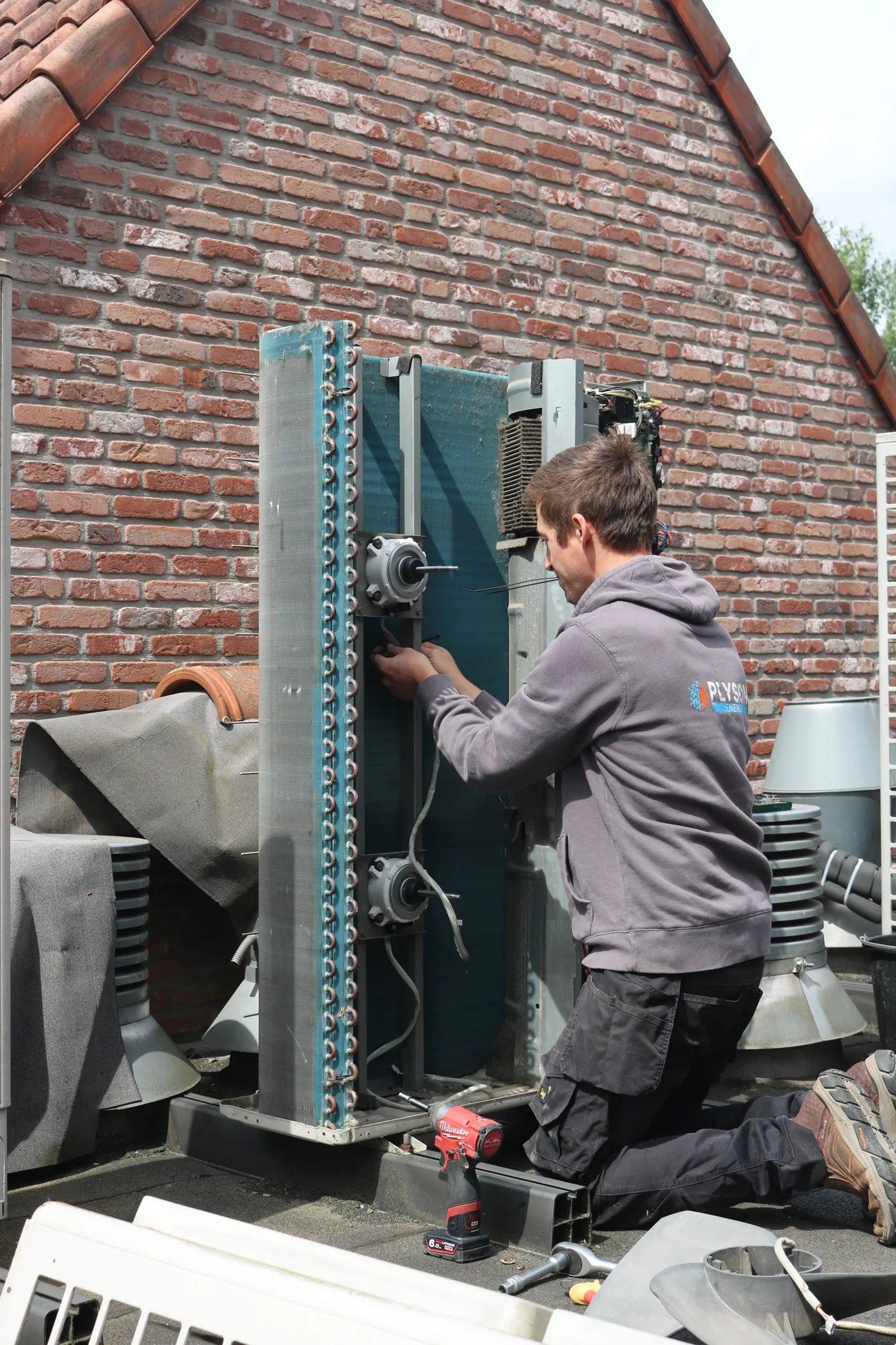 Robin werkt aan een geopende buitenunit, met het Plyson Energy-logo op zijn werkkledij